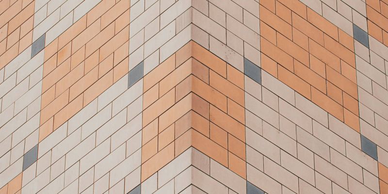 A building corner with a geometric pattern of orange, beige, and blue tiles forming a diamond design.