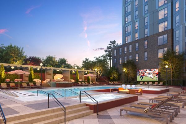 Outdoor pool area with lounge chairs, umbrellas, and a large screen showing a football game at sunset.