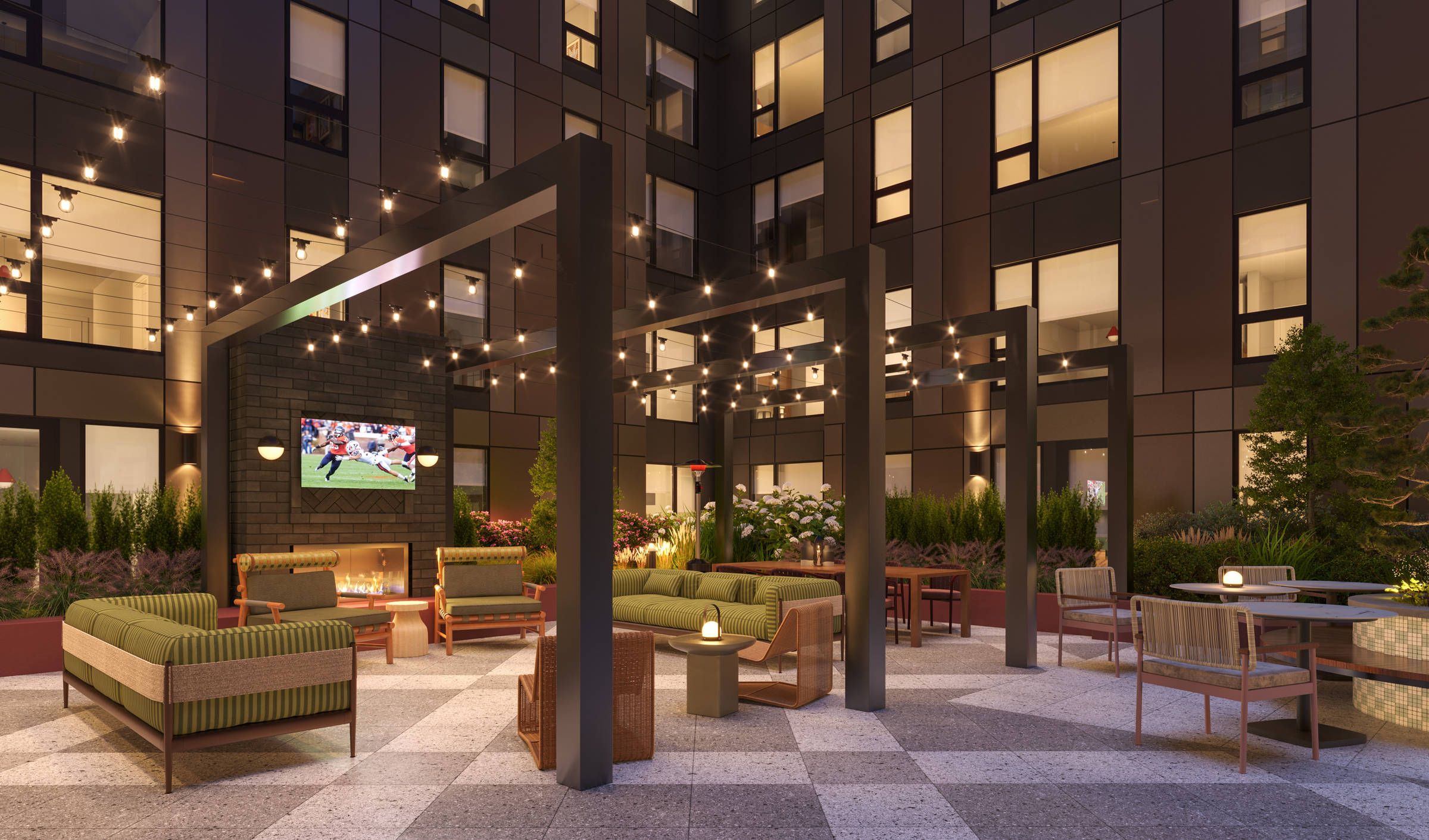 Modern outdoor lounge with green sofas, string lights, firepit, TV screen, and plants surrounded by tall windows.