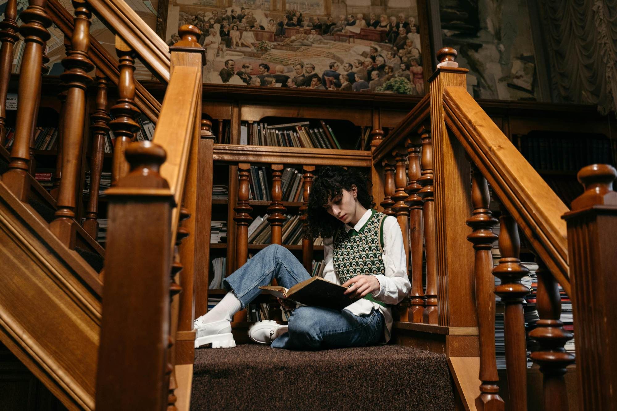 Student reading on a staircase surrounded by wooden railings and bookshelves near VERVE Charlottesville.