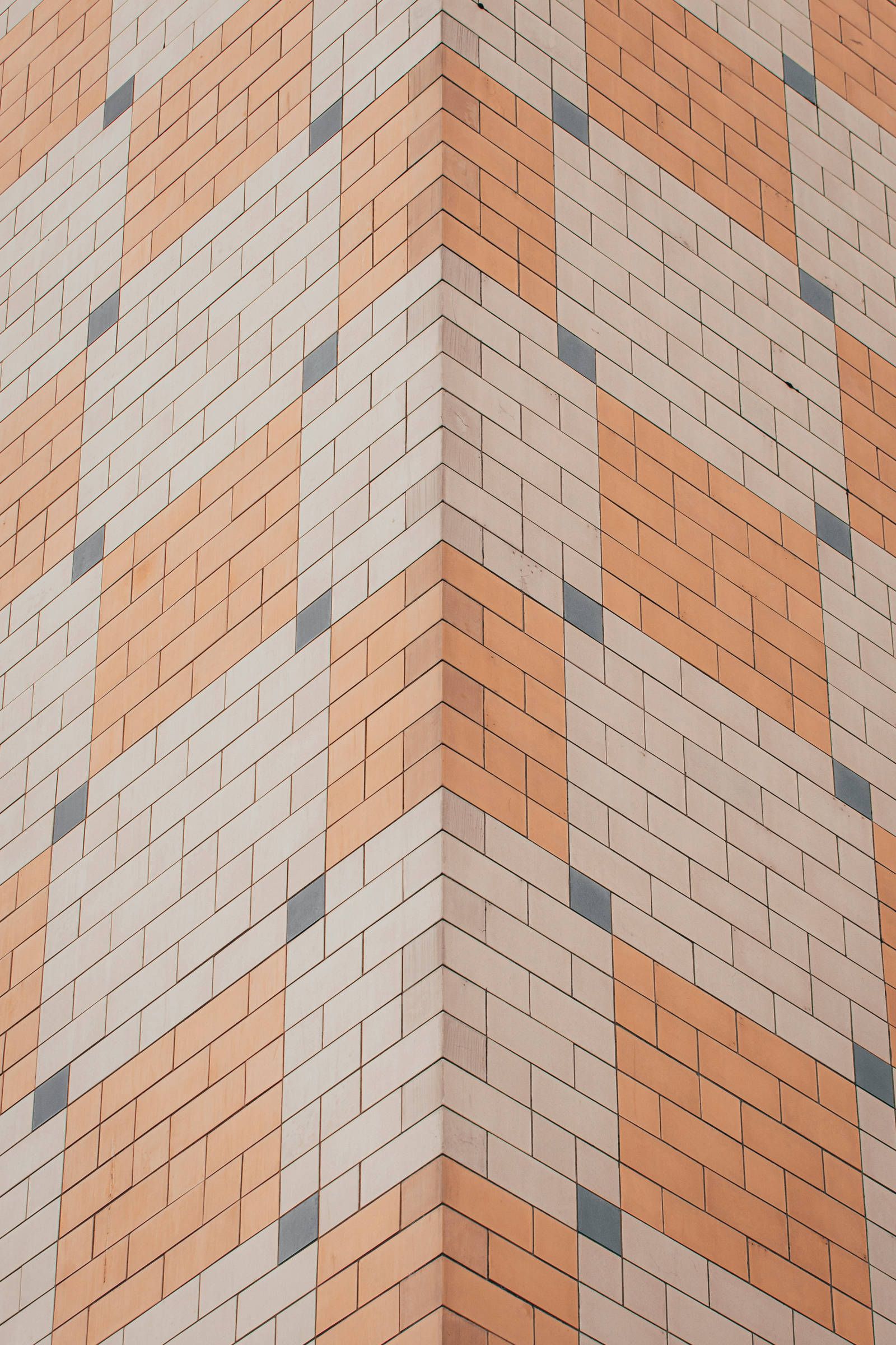 A building corner with a geometric pattern of orange, beige, and blue tiles forming a diamond design.