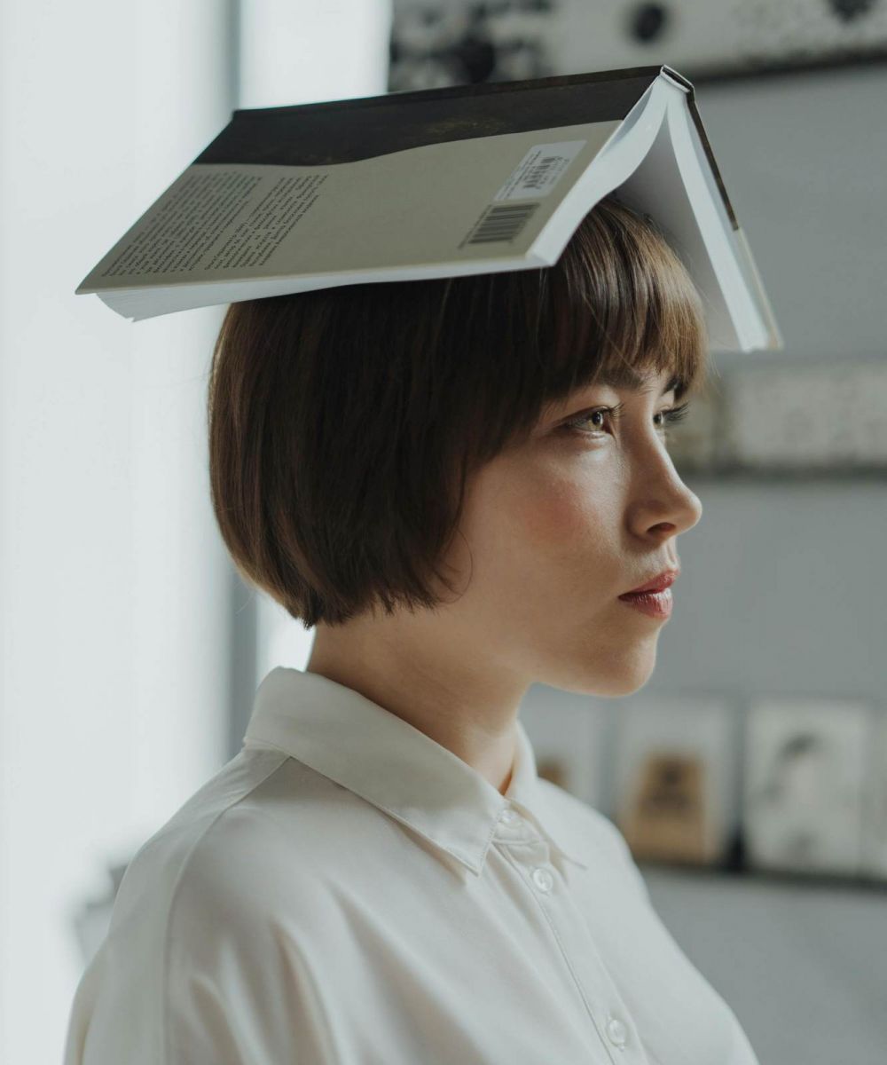 Student playfully balancing an open book on their head inside a study space at VERVE Charlottesville.