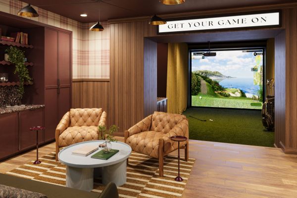 A cozy lounge with tan chairs faces a golf simulator; a "Get Your Game On" sign hangs above.