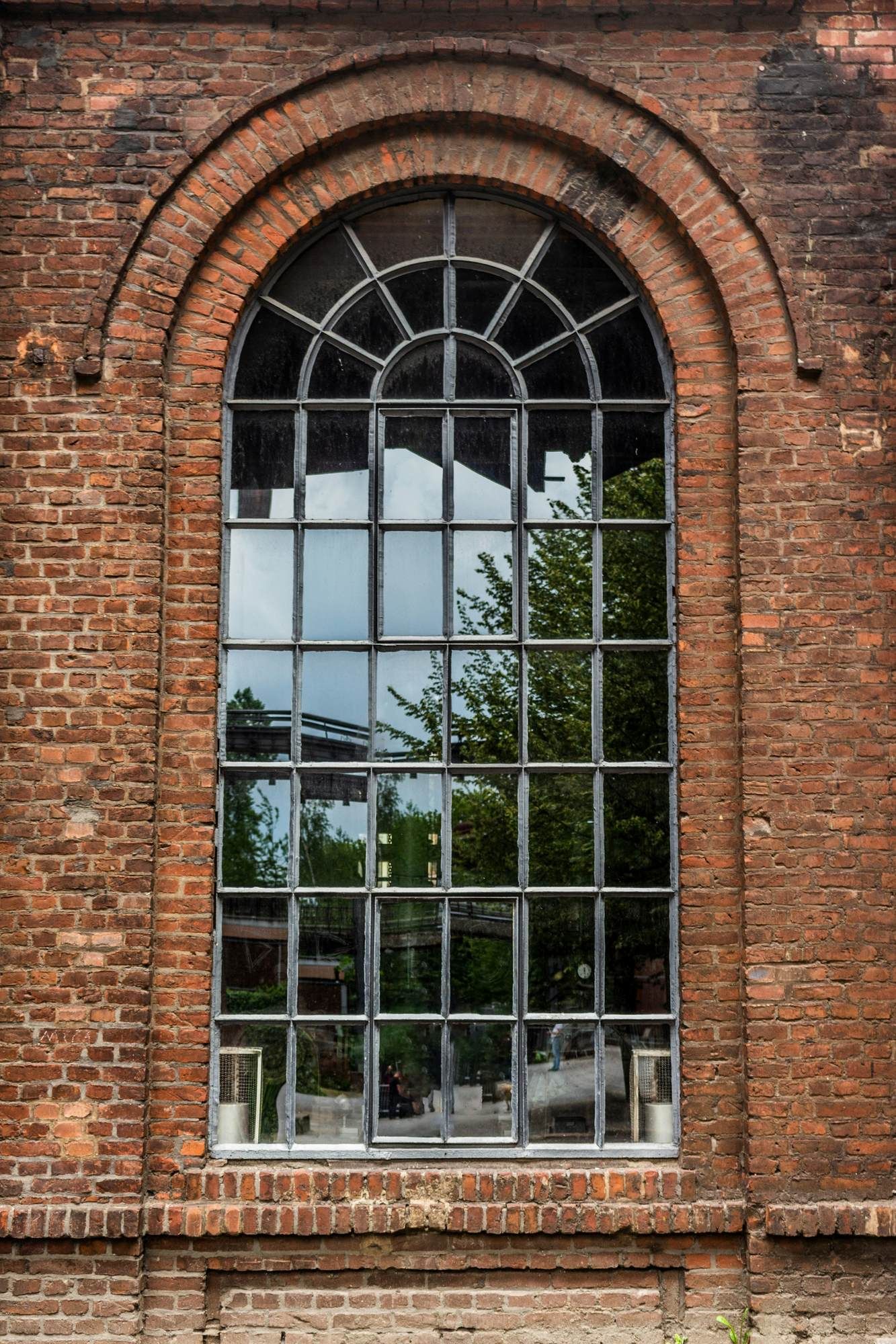 Large arched window set in a brick exterior, reflecting trees and the surrounding area near VERVE Charlottesville.